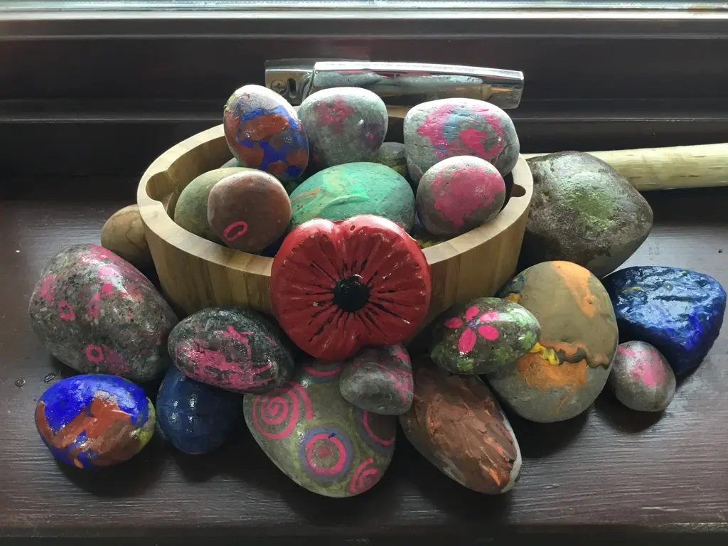 Wooden bowl of brightly painted pebbles and stones sitting on a dark window sill